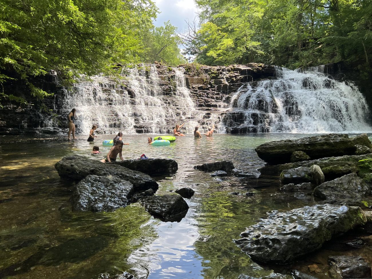 Families swimming in the pool below a wide Tennessee waterfall